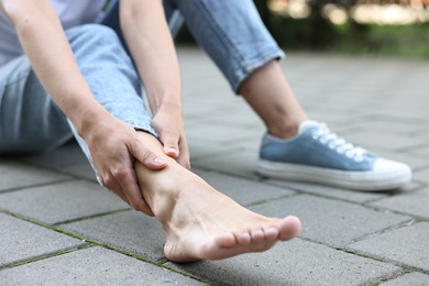 Photo of Woman suffering from foot pain outdoors, closeup