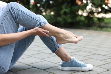 Photo of Woman suffering from foot pain outdoors, closeup