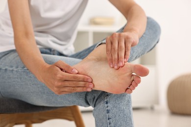 Photo of Woman suffering from foot pain at home, closeup