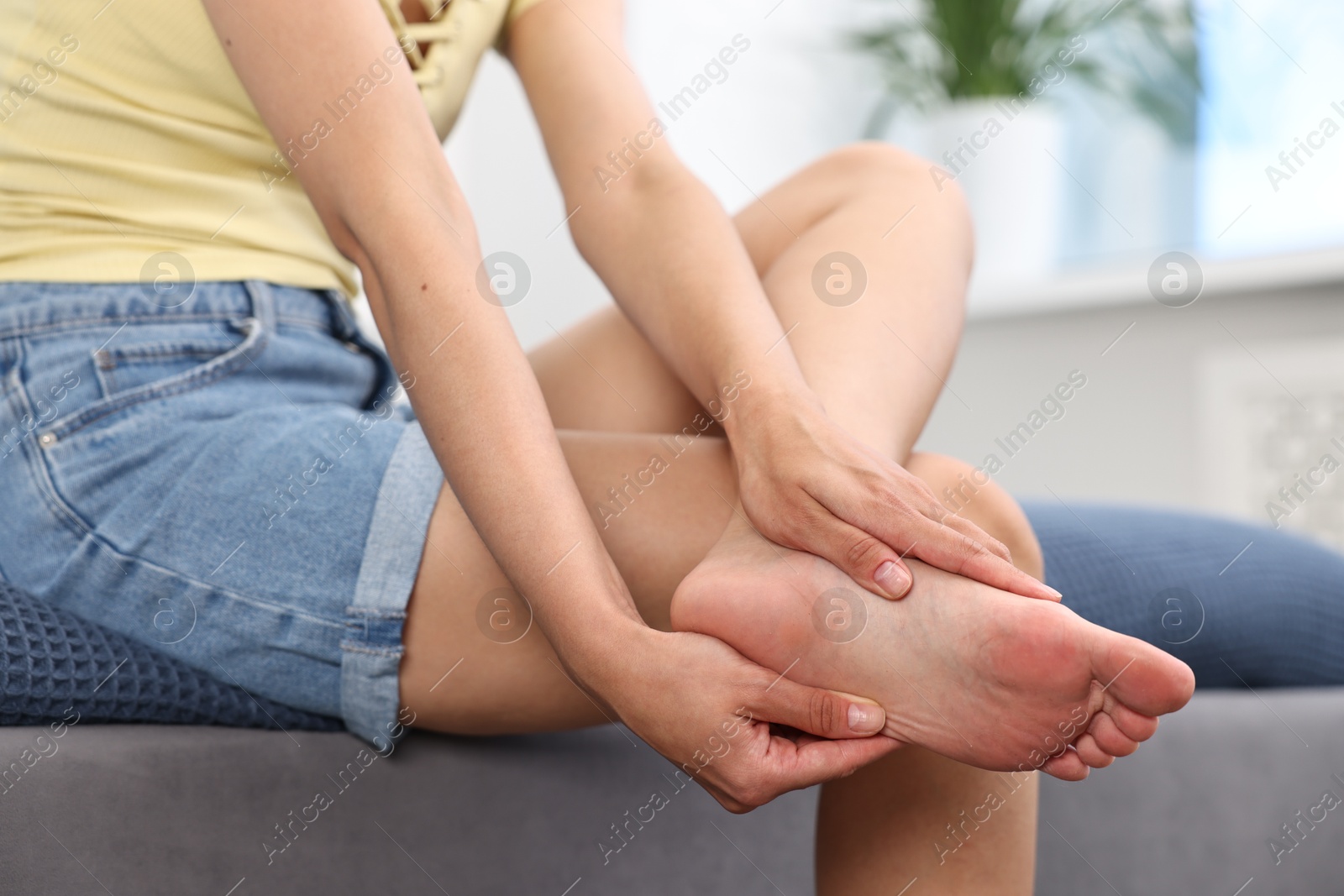 Photo of Woman suffering from foot pain on bed at home, closeup