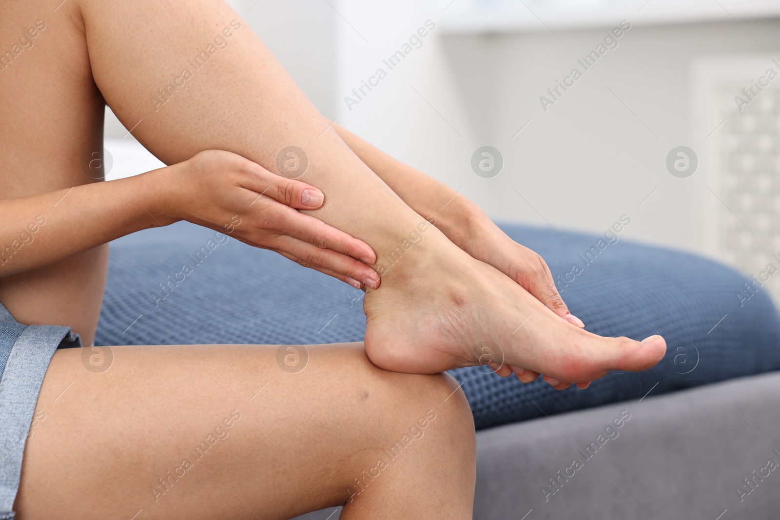 Photo of Woman suffering from foot pain on bed at home, closeup