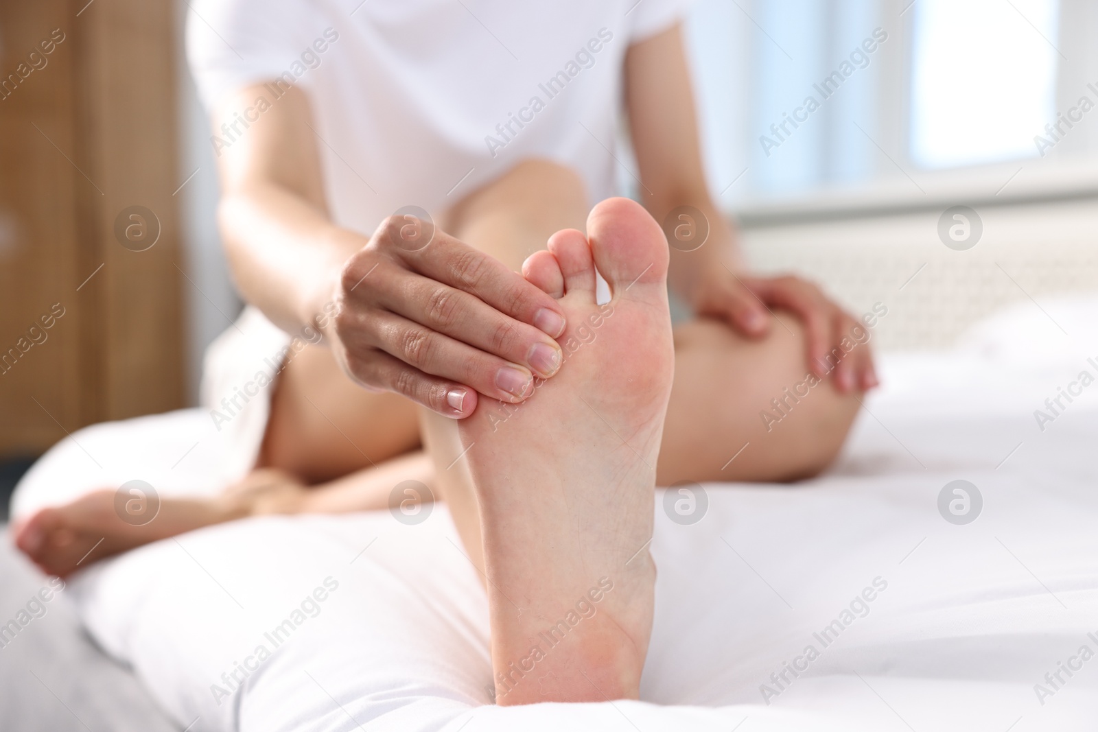 Photo of Woman suffering from foot pain on bed at home, closeup