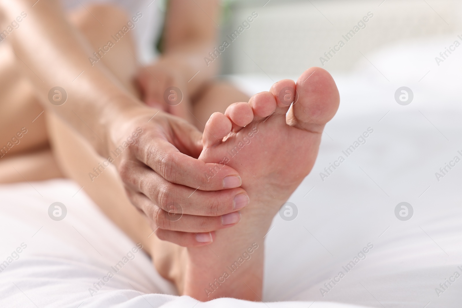 Photo of Woman suffering from foot pain on bed at home, closeup