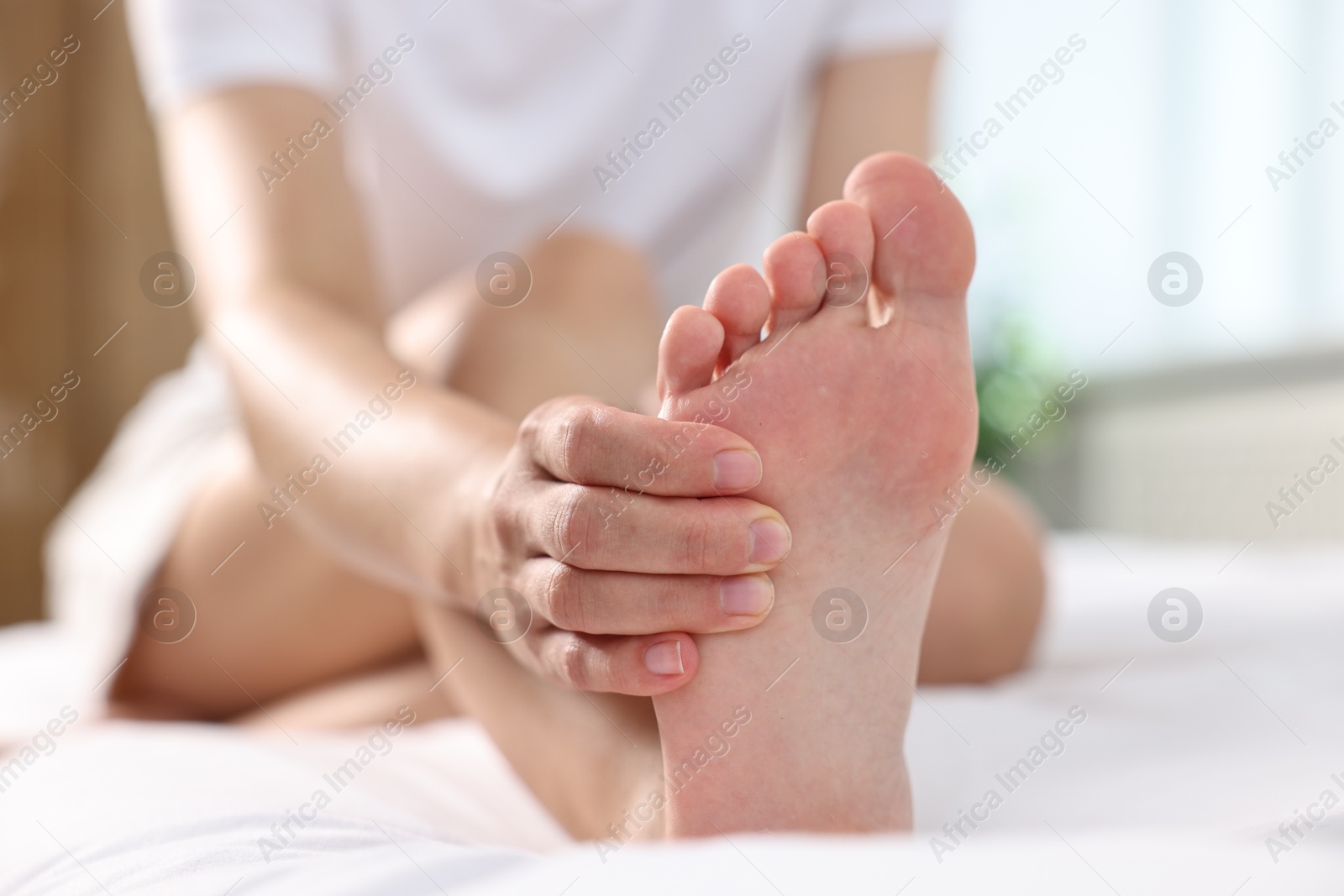 Photo of Woman suffering from foot pain on bed at home, closeup