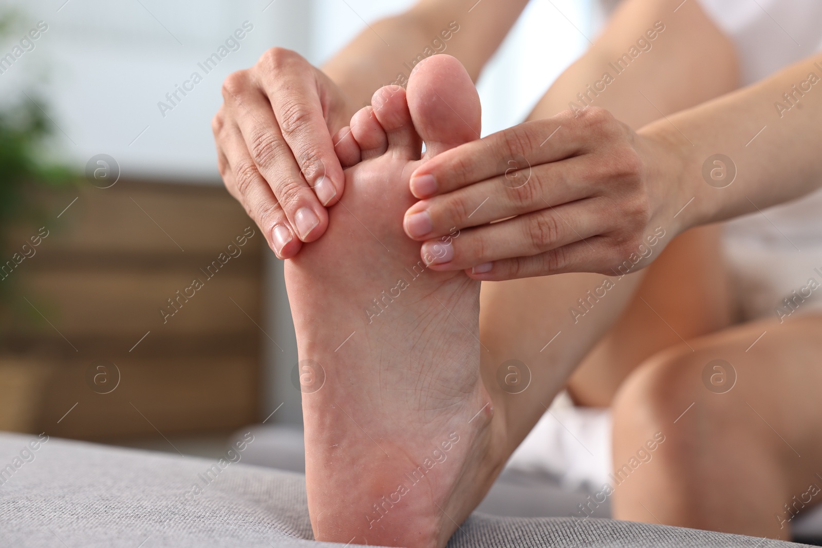 Photo of Woman suffering from foot pain on bed at home, closeup