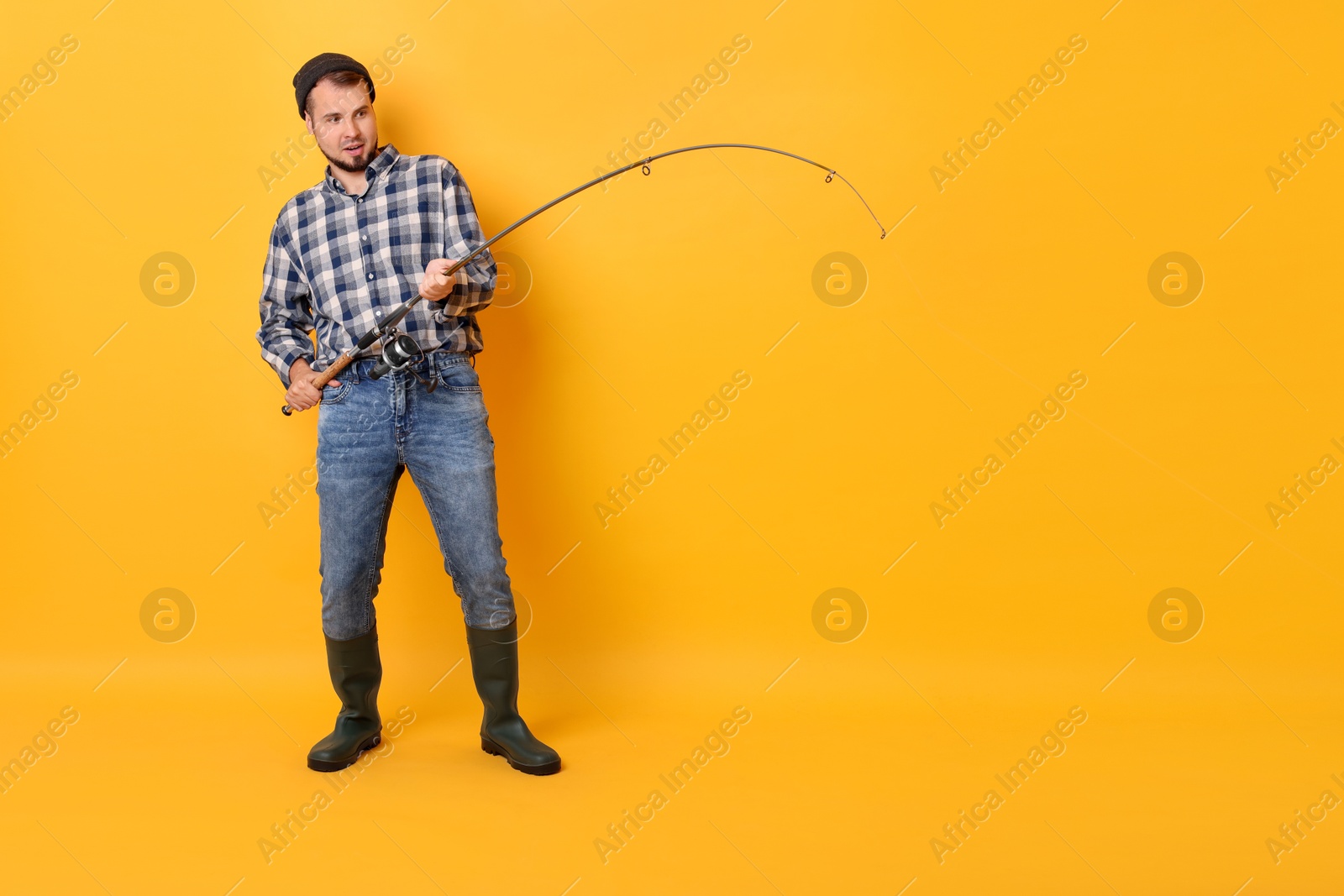 Photo of Fisherman with rod fishing on orange background, space for text