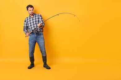 Fisherman with rod fishing on orange background, space for text