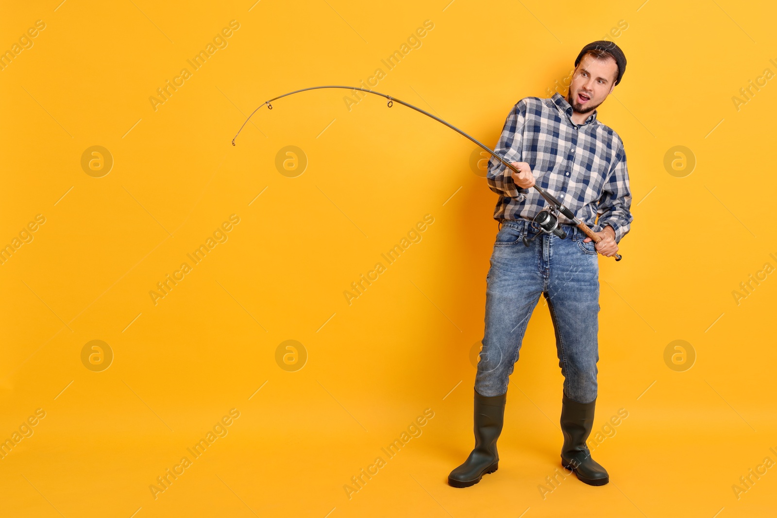 Photo of Emotional fisherman with rod fishing on orange background, space for text