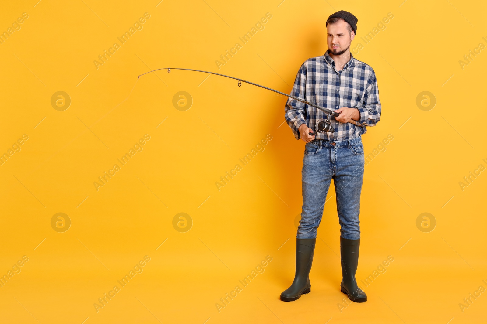 Photo of Fisherman with rod fishing on orange background, space for text