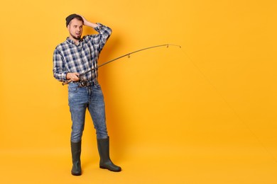 Photo of Fisherman with rod fishing on orange background, space for text