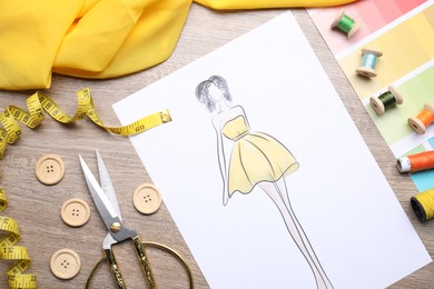 Photo of Sketch of stylish clothes and other fashion designer`s supplies on wooden table, flat lay