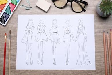 Photo of Sketch of stylish clothes and other fashion designer`s supplies on wooden table, flat lay