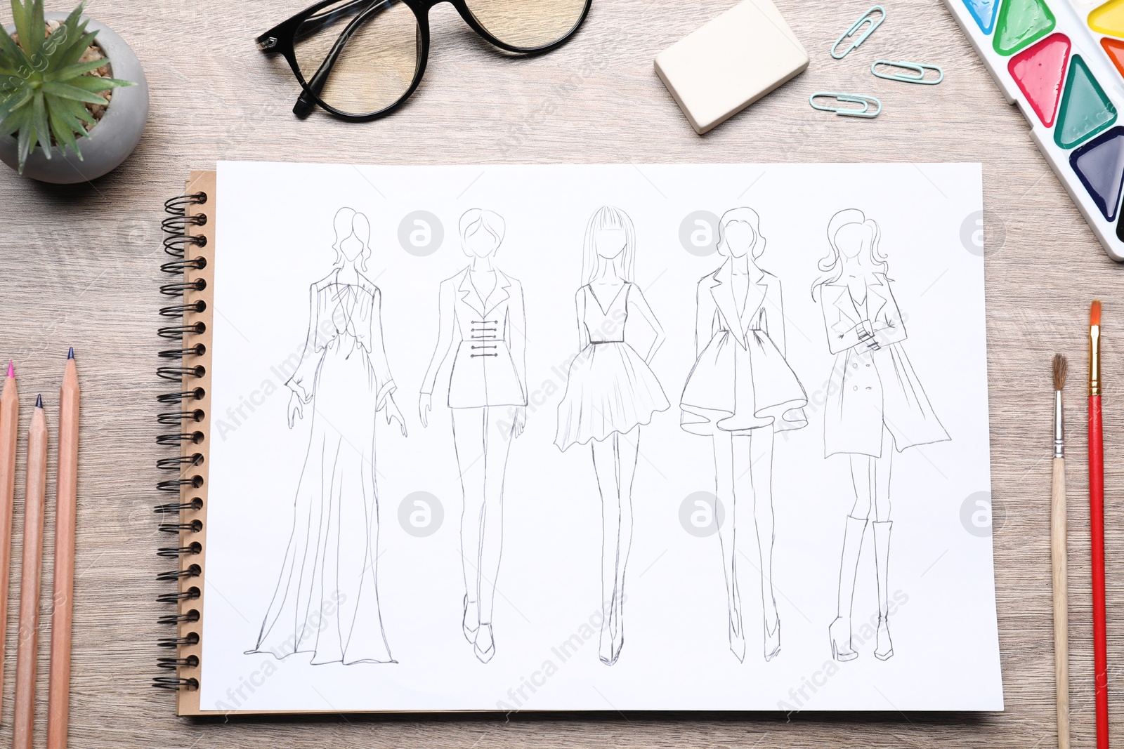 Photo of Sketch of stylish clothes and other fashion designer`s supplies on wooden table, flat lay