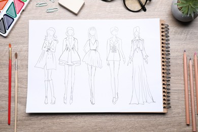 Photo of Sketch of stylish clothes and other fashion designer`s supplies on wooden table, flat lay