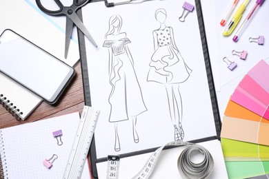 Sketch of stylish clothes and other fashion designer`s supplies on wooden table, flat lay