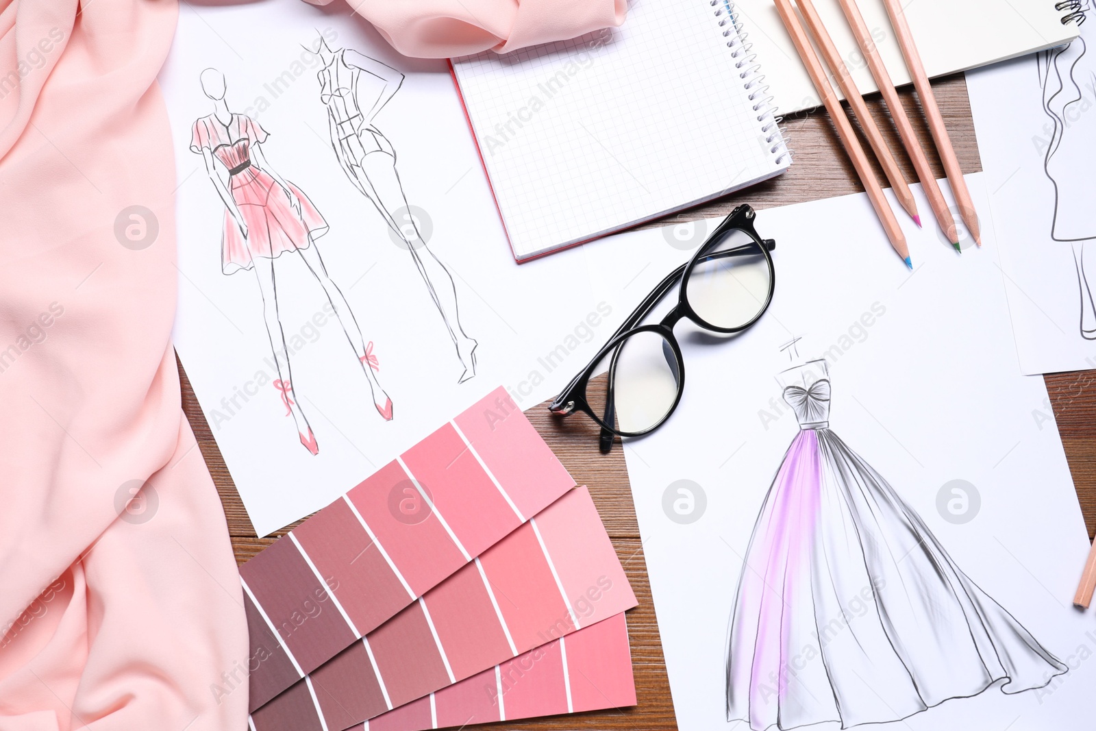 Photo of Sketches of stylish clothes and other fashion designer`s supplies on wooden table, flat lay