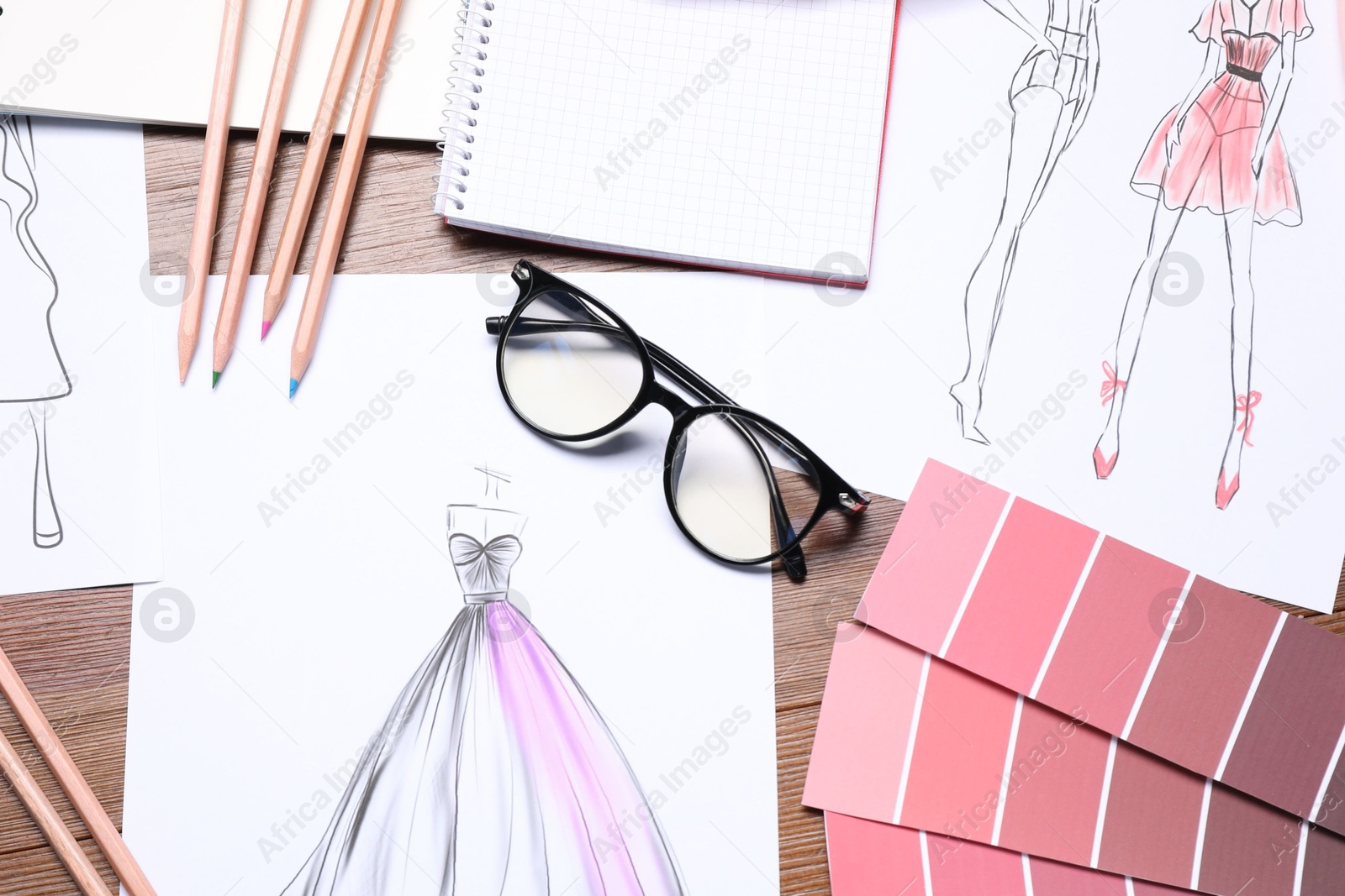 Photo of Sketches of stylish clothes and other fashion designer`s supplies on wooden table, flat lay