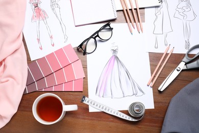 Photo of Sketches of stylish clothes and other fashion designer`s supplies on wooden table, flat lay