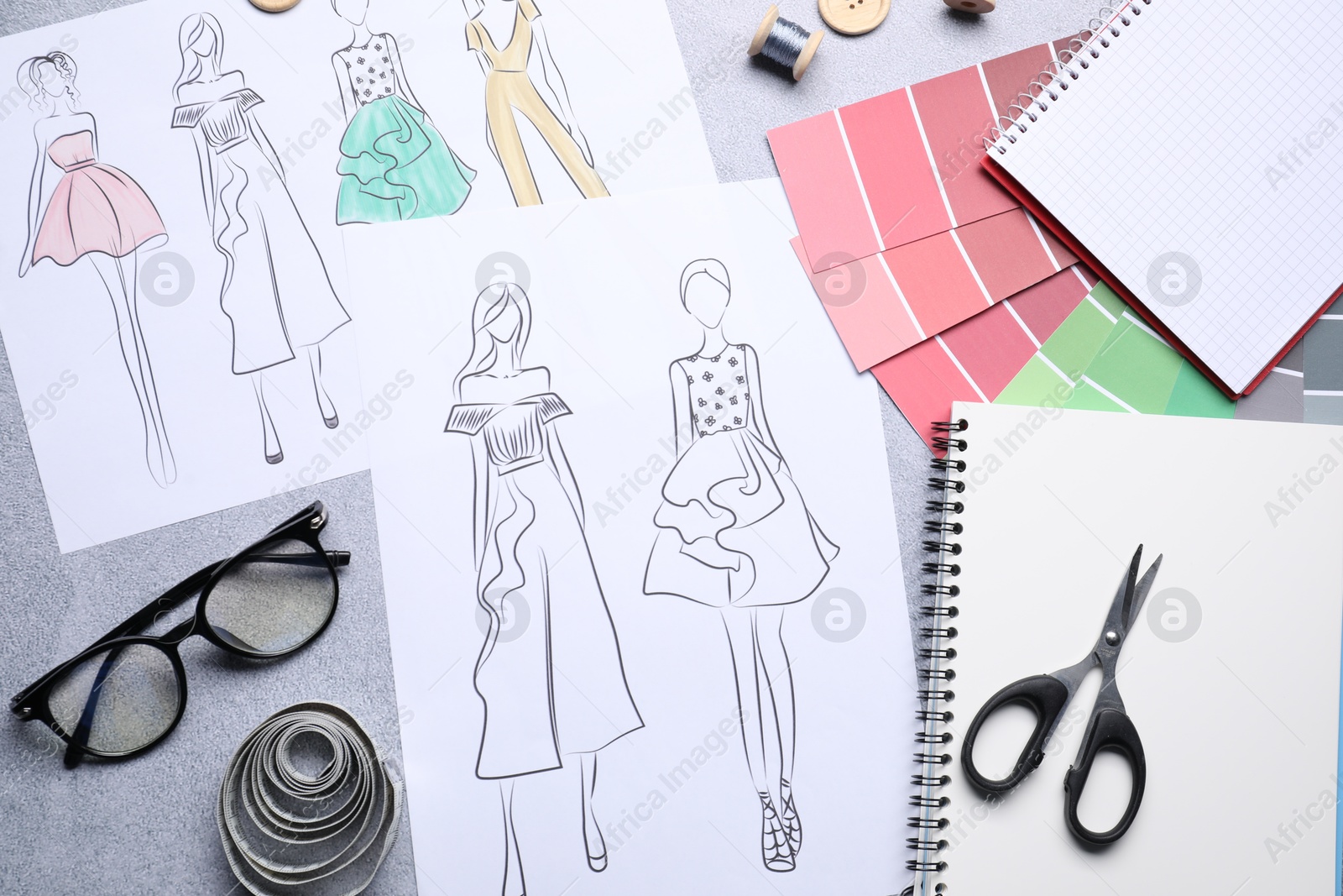 Photo of Sketches of stylish clothes and other fashion designer`s supplies on grey table, flat lay