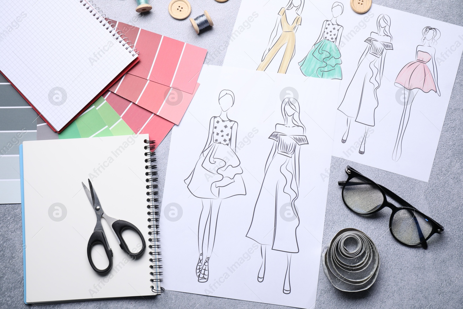 Photo of Sketches of stylish clothes and other fashion designer`s supplies on grey table, flat lay