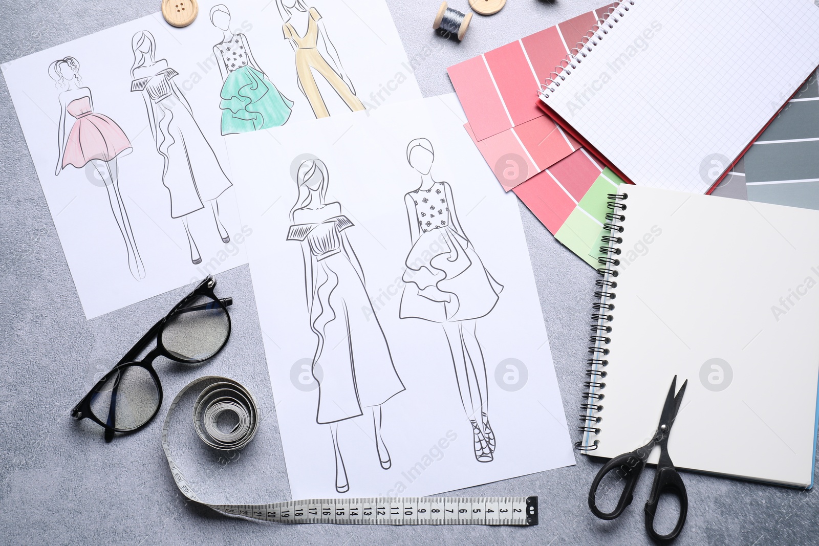 Photo of Sketches of stylish clothes and other fashion designer`s supplies on grey table, flat lay