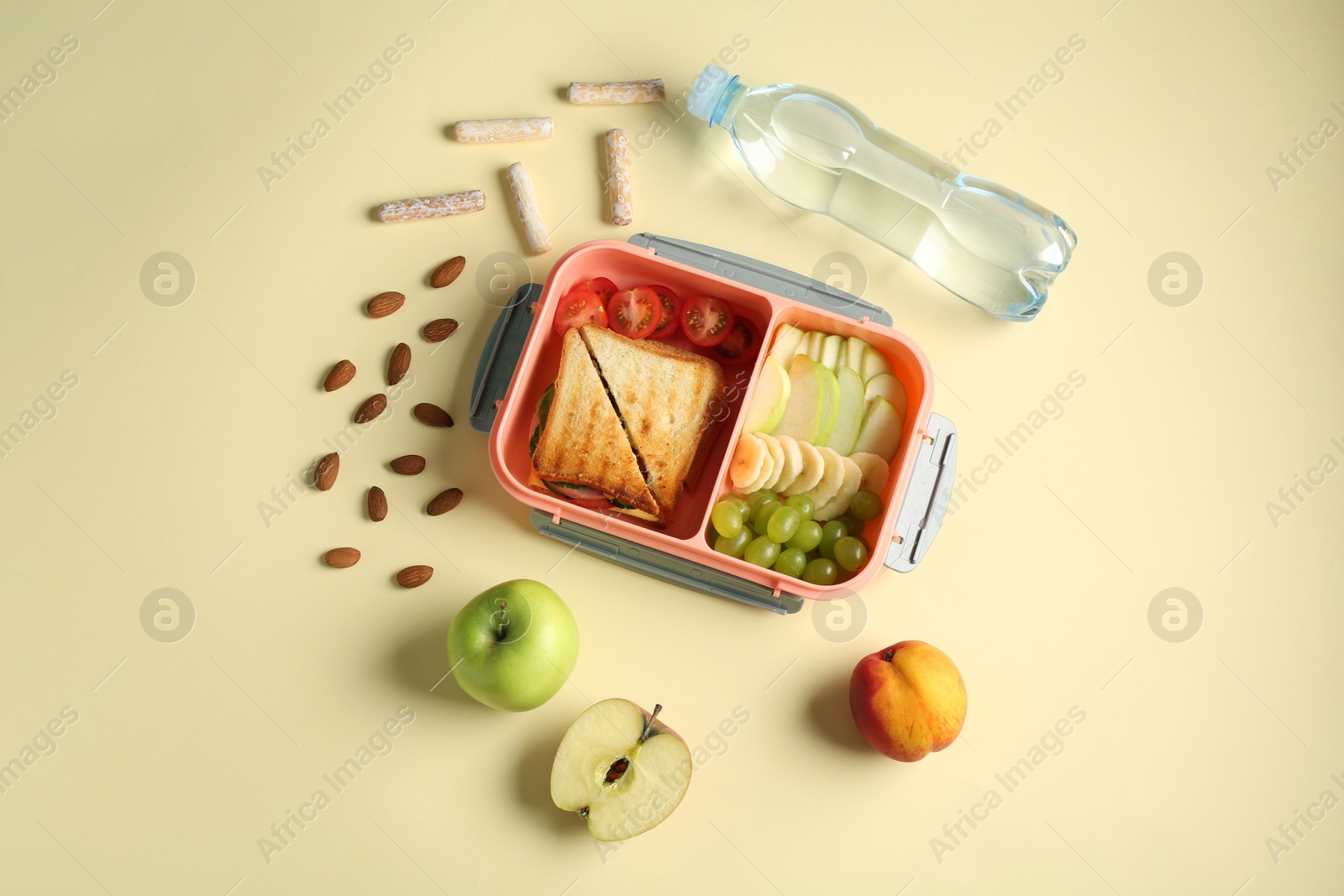 Photo of Lunch box with snacks and bottle of water on yellow table, flat lay