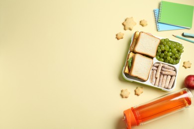 Photo of Lunch box with snacks, bottle and stationery on yellow table, flat lay. Space for text