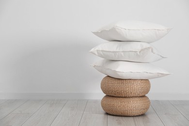 Photo of Stack of clean pillows on wicker poufs near white wall. Space for text