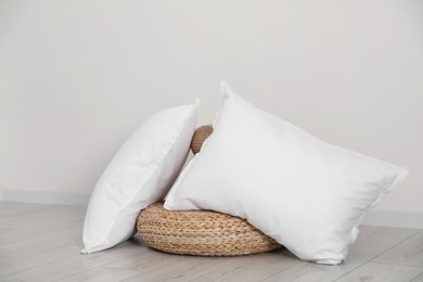 Photo of Clean pillows and wicker poufs on floor near white wall