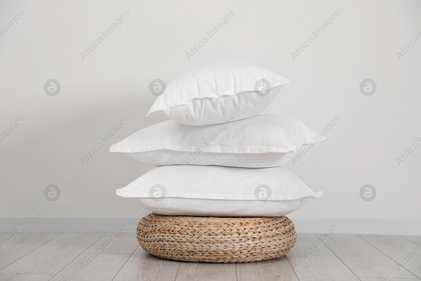 Photo of Stack of clean pillows on wicker pouf near white wall