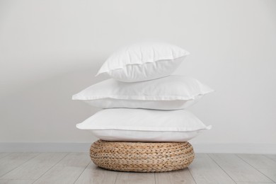 Photo of Stack of clean pillows on wicker pouf near white wall