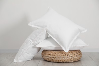 Photo of Clean pillows and wicker pouf on floor near white wall