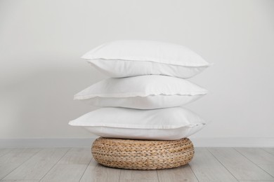 Photo of Stack of clean pillows on wicker pouf near white wall