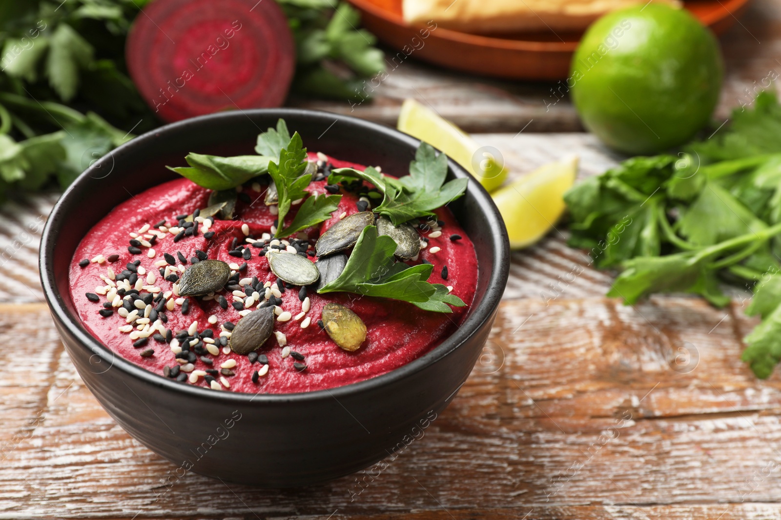 Photo of Tasty beetroot hummus in bowl and products on wooden table, closeup