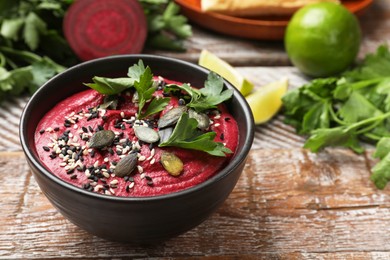 Tasty beetroot hummus in bowl and products on wooden table, closeup