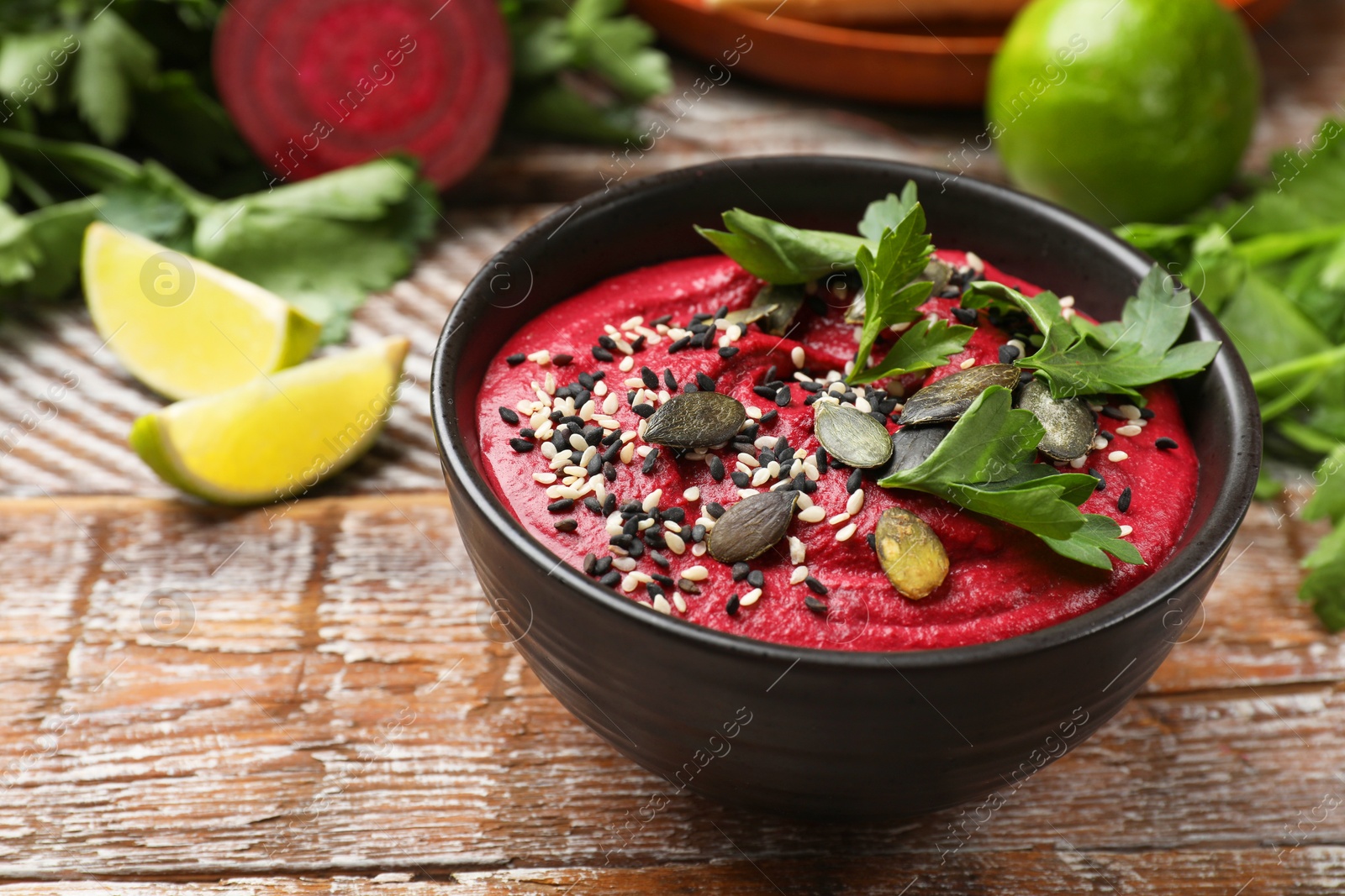 Photo of Tasty beetroot hummus in bowl and products on wooden table, closeup