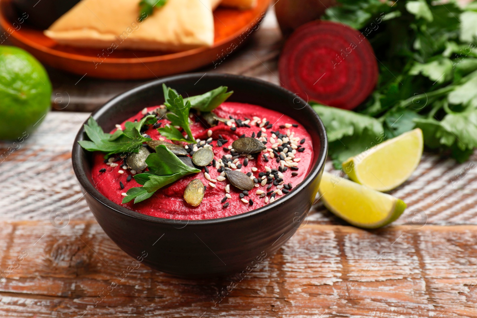 Photo of Tasty beetroot hummus in bowl and products on wooden table