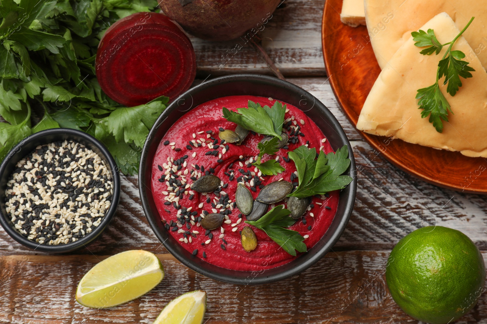 Photo of Tasty beetroot hummus in bowl and products on wooden table, flat lay