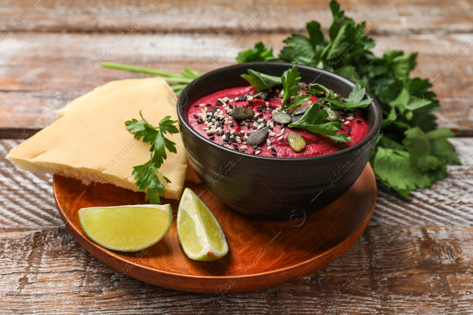 Photo of Tasty beetroot hummus in bowl and products on wooden table