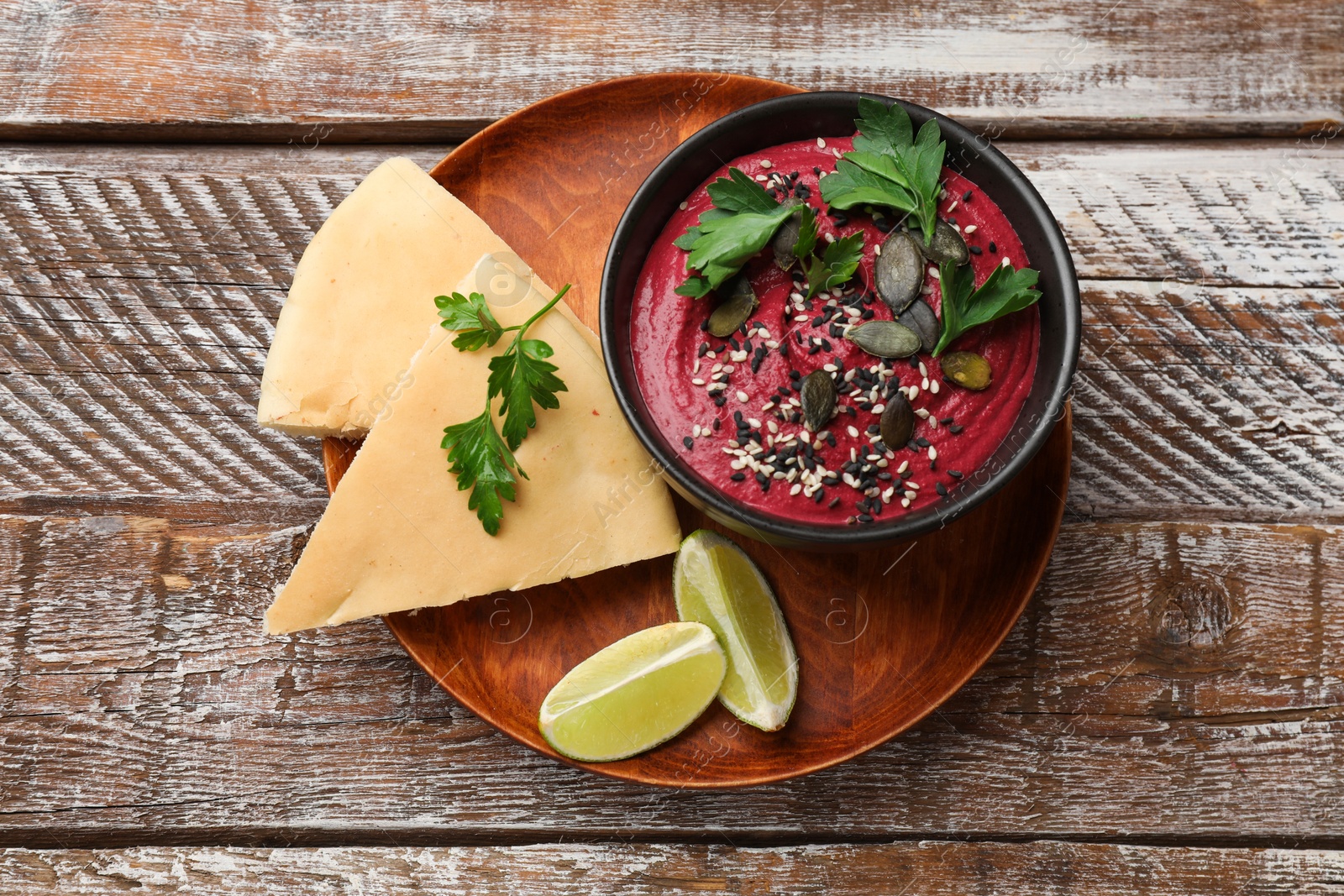 Photo of Tasty beetroot hummus in bowl and products on wooden table, top view