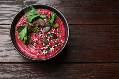 Tasty beetroot hummus, parsley and seeds in bowl on wooden table, top view. Space for text