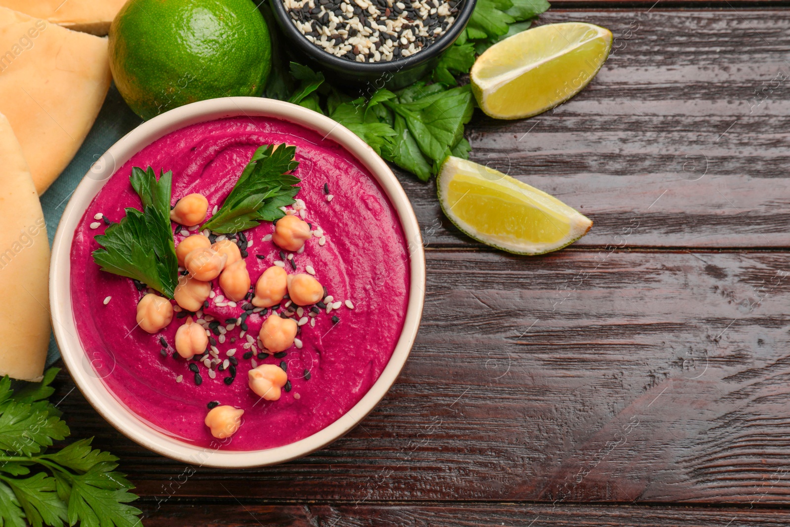 Photo of Tasty beetroot hummus in bowl and products on wooden table, flat lay. Space for text