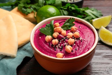 Photo of Tasty beetroot hummus in bowl and products on wooden table, closeup