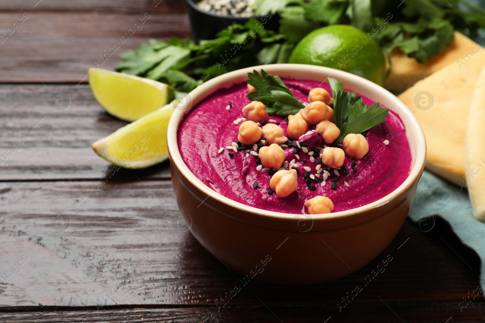 Photo of Tasty beetroot hummus in bowl and products on wooden table, closeup