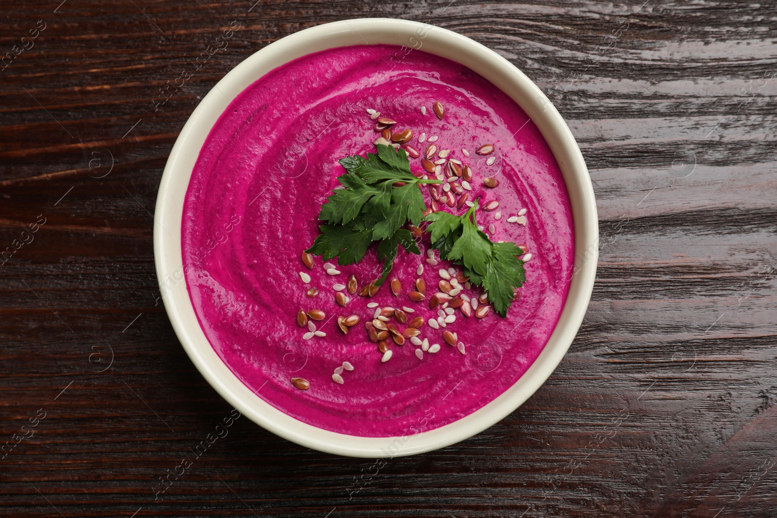 Photo of Tasty beetroot hummus, parsley and seeds in bowl on wooden table, top view