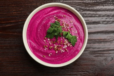 Photo of Tasty beetroot hummus, parsley and seeds in bowl on wooden table, top view