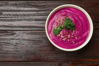 Tasty beetroot hummus, parsley and seeds in bowl on wooden table, top view. Space for text