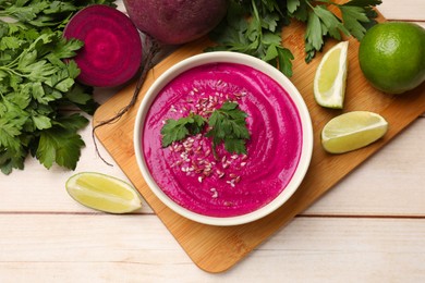 Photo of Tasty beetroot hummus in bowl and products on light wooden table, flat lay