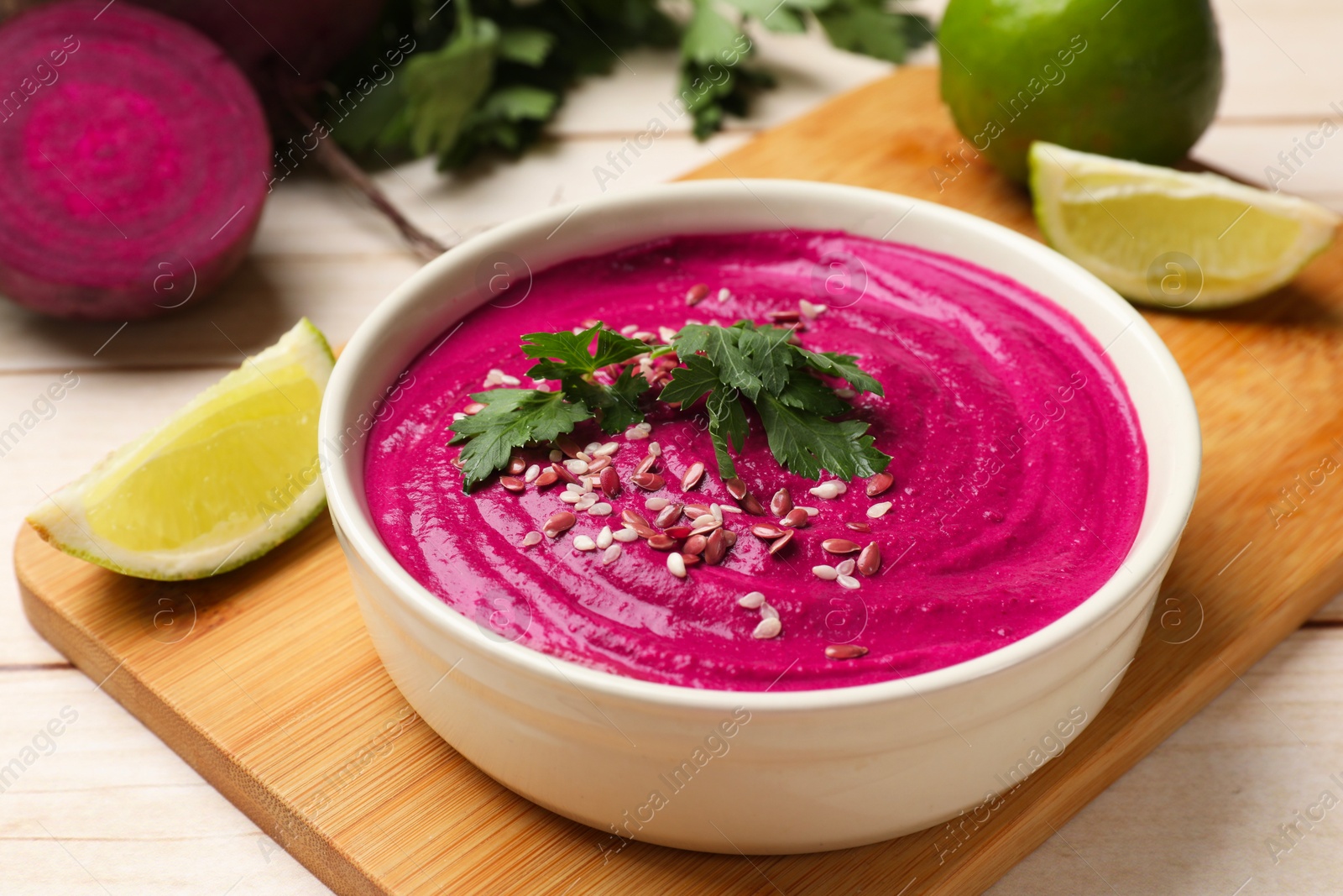 Photo of Tasty beetroot hummus in bowl and products on light wooden table, closeup