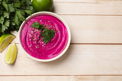 Photo of Tasty beetroot hummus, parsley and lime in bowl on light wooden table, flat lay. Space for text